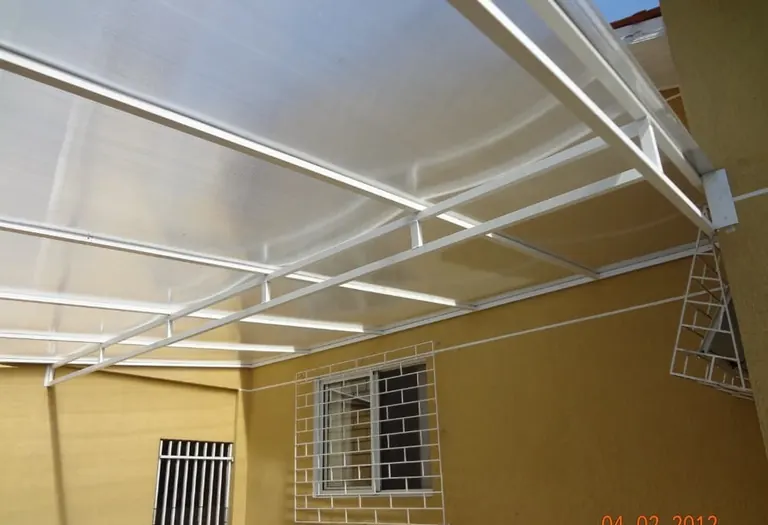 Cobertura reta de policarbonato leitoso com estrutura branca cobrindo área externa lateral