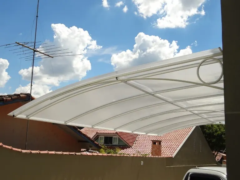 Cobertura curva de policarbonato leitoso em balanço protegendo garagem residencial